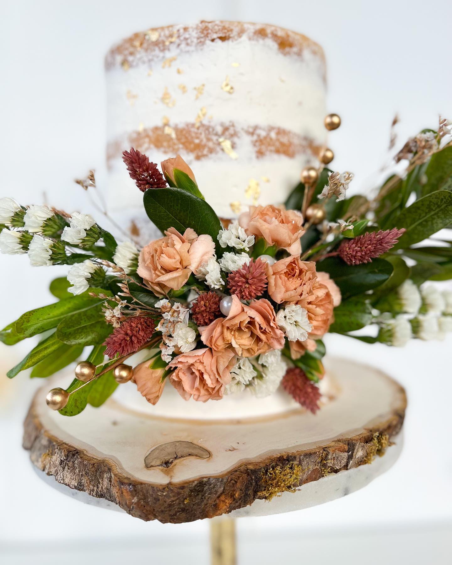 Naked tier cake with peach garden florals on a wood slice